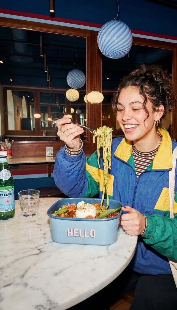 Smiling woman twirling pasta at a marble cafe table
