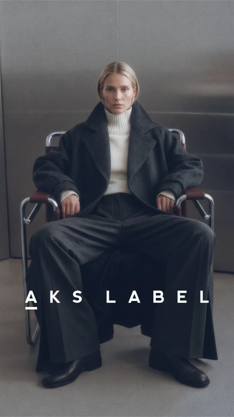 AKS Label seated model in a black suit and pale roll-neck top