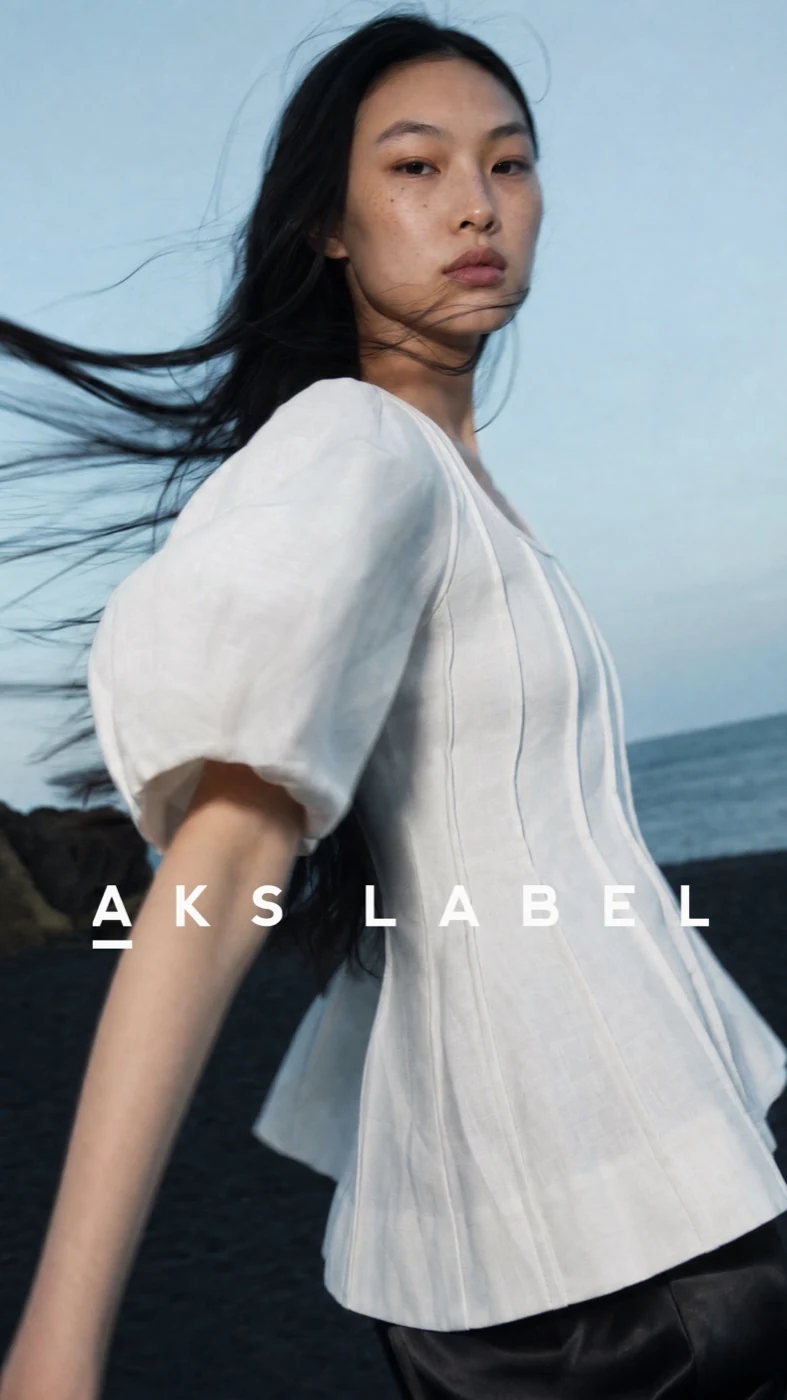 AKS Label model in a white blouse against a blue sky