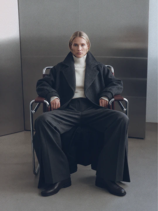 Seated fashion portrait in a dark tailored coat and long skirt.