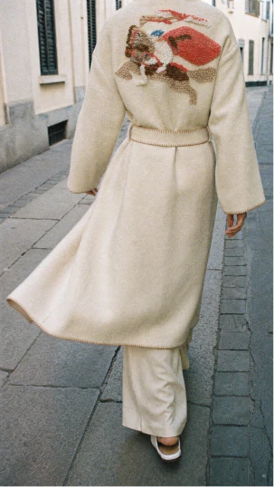 Street-style fashion portrait of a cream embroidered coat from behind.