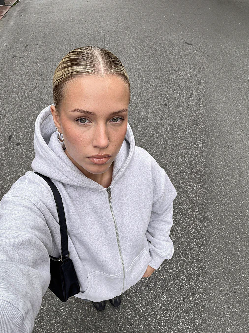 Overhead street-style selfie in a pale grey hoodie.