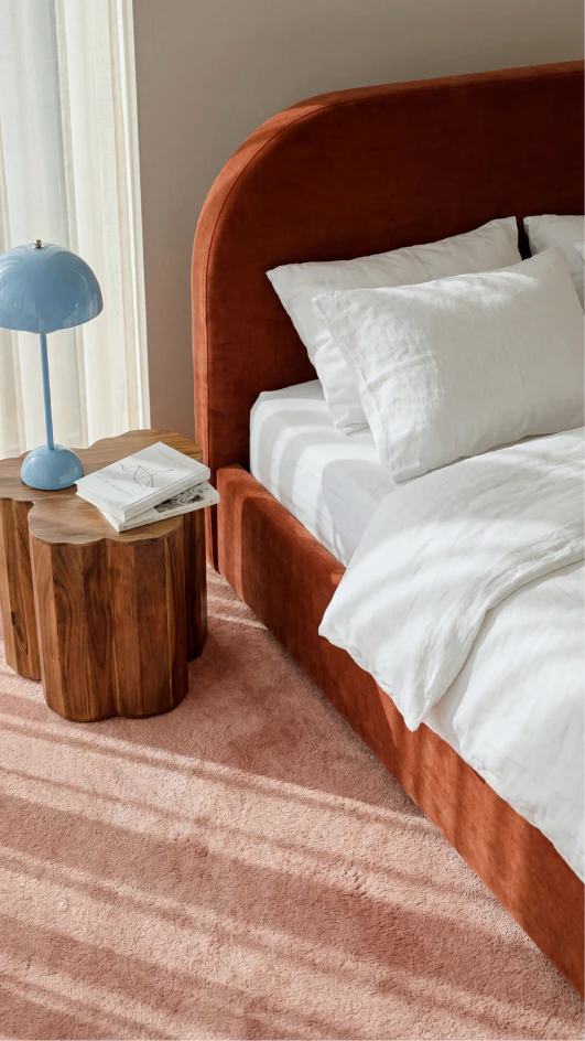 Rust-coloured upholstered bed in a bright bedroom with a patterned rug.