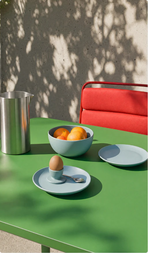 Green sculptural table and red chair in dappled sunlight.