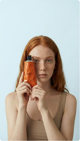 Red-haired woman holding an amber wellness bottle against a pale blue background.