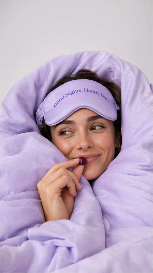 Woman in lavender bedding wearing a sleep mask.