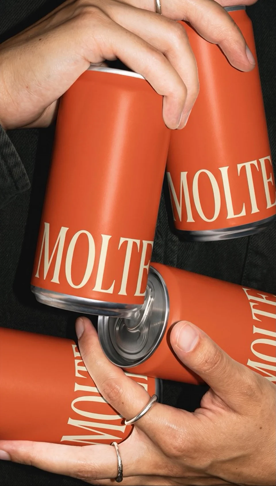 Hands holding bright orange MOLTE cans against black clothing.