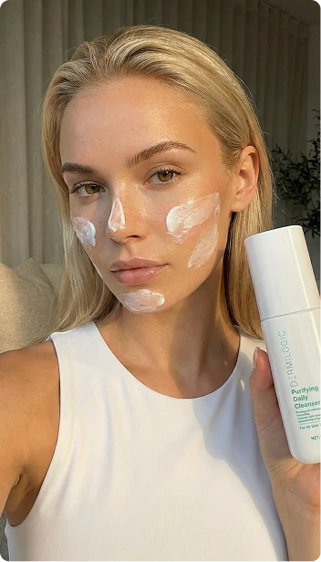 Woman applying skincare cream while holding a white bottle.