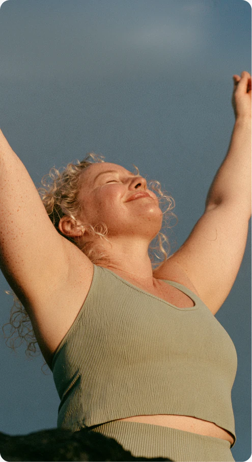 Woman in workout clothing stretching her arms against a blue-grey background.