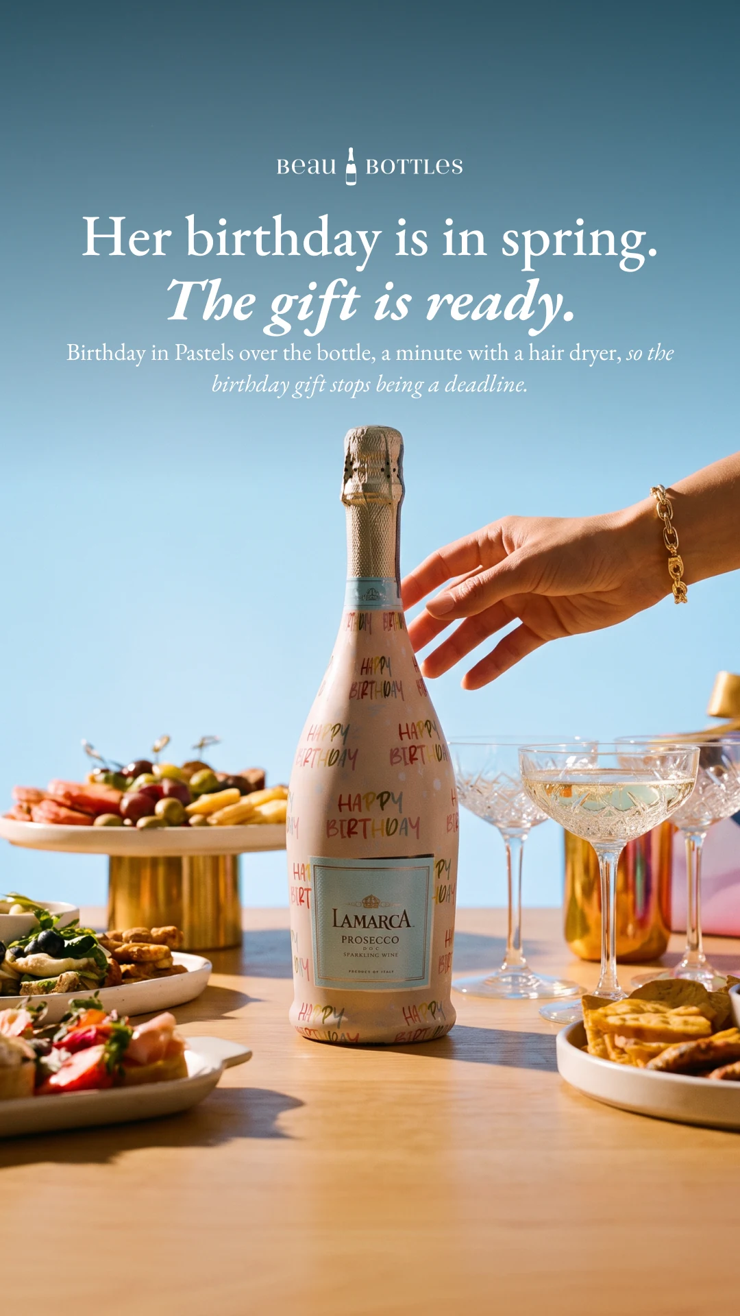A Beau Bottles birthday prosecco bottle on a sunlit table beneath the campaign headline.
