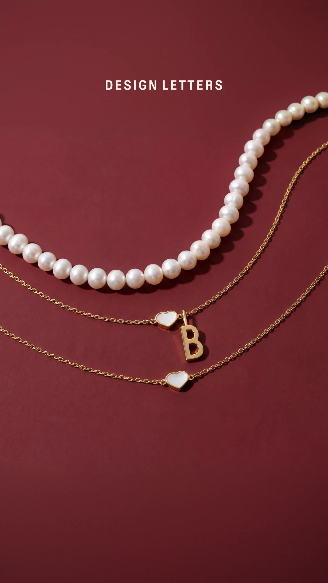 Design Letters pearls and gold chains arranged on a burgundy background.